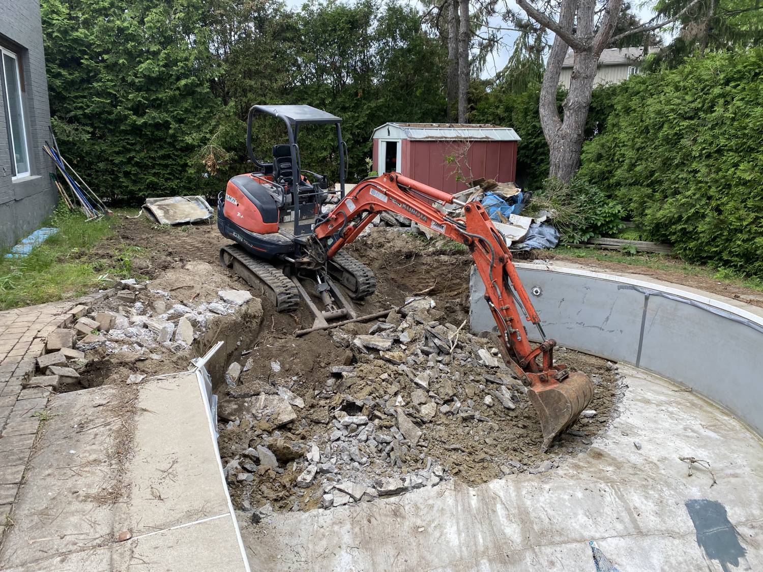 Kubota mini excavator breaking and removing concrete during inground pool demolition and backyard excavation project
