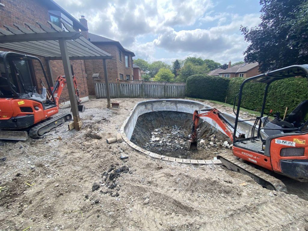 an excavator in the process of dismantling a concrete swimming pool
