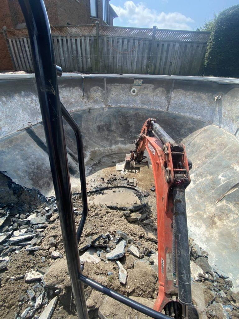 an excavator in the process of dismantling a concrete swimming pool