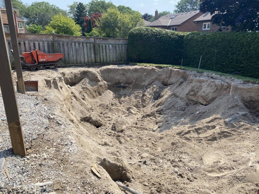 Excavated backyard after full inground pool removal with compact tracked dumper on site