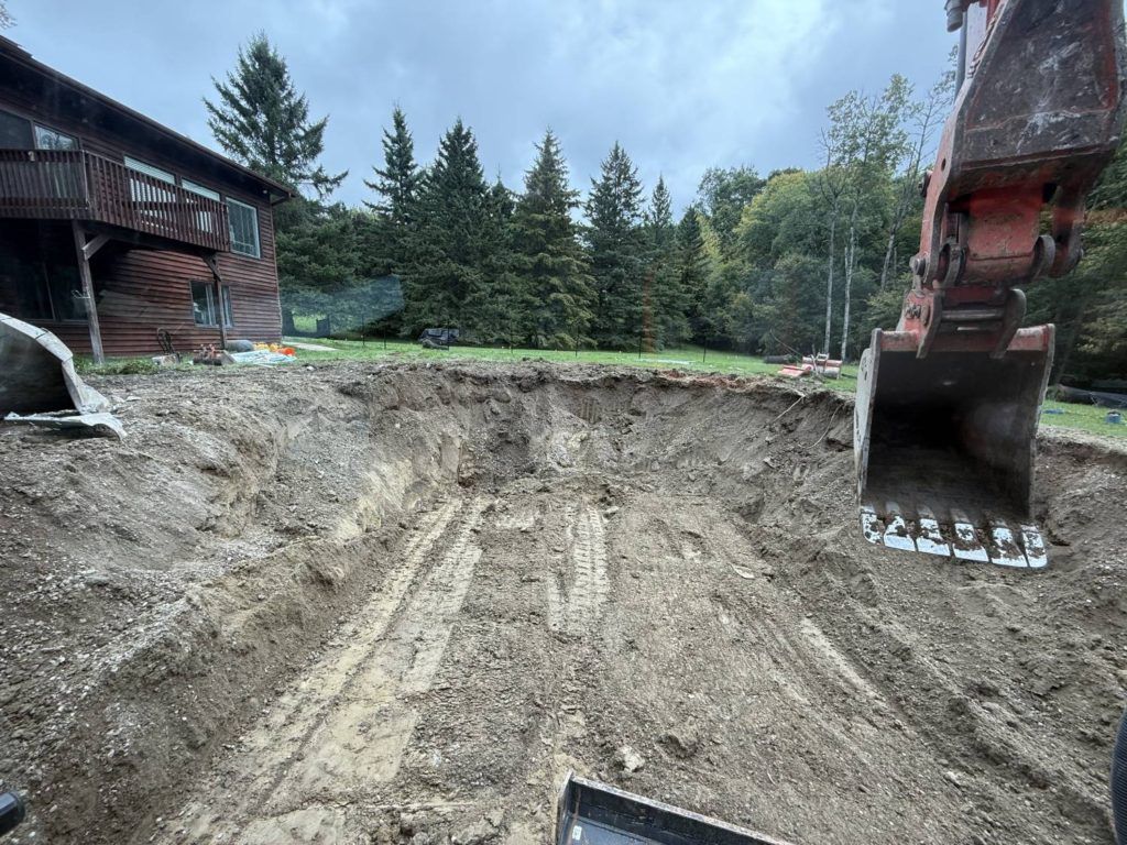 Excavated backyard site after full inground pool demolition with excavator bucket visible in foreground