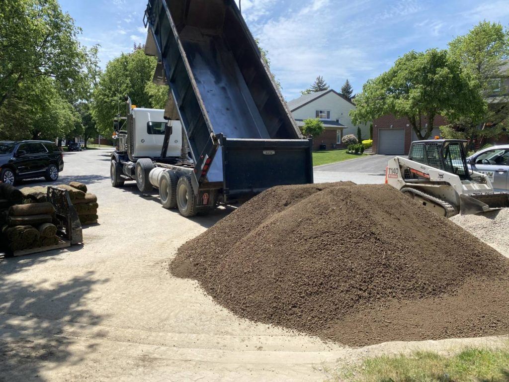 a truck dumping sand at the edge of a garden