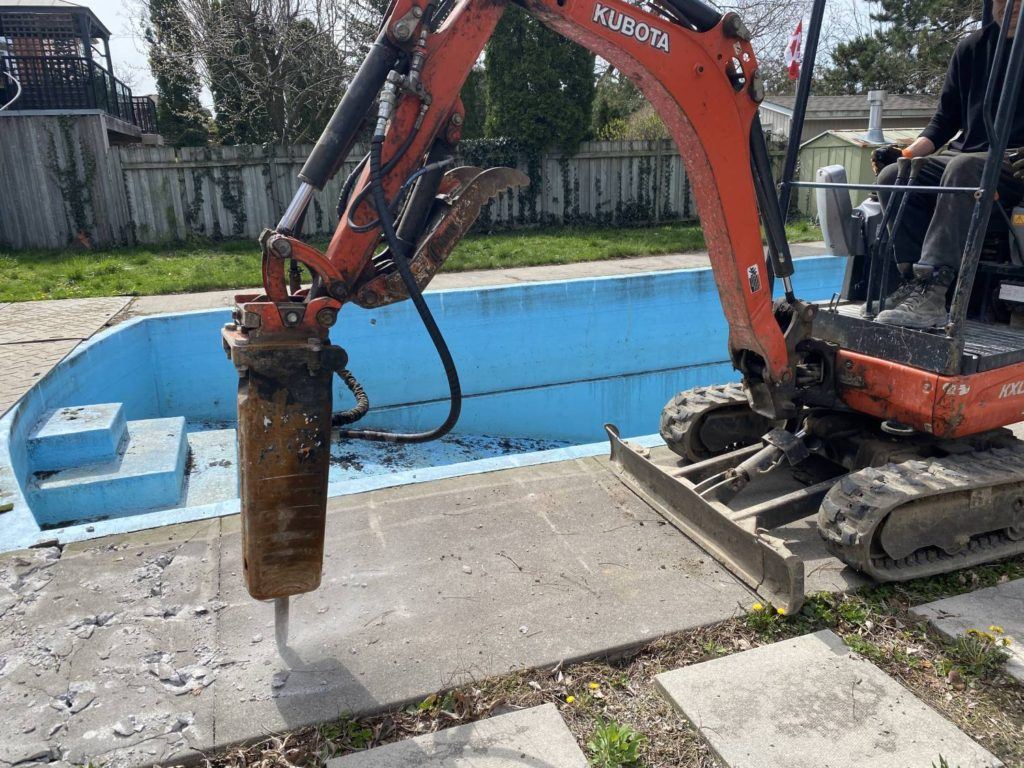 a kubota equipped with a jack-hammer breaking up a swimming pool