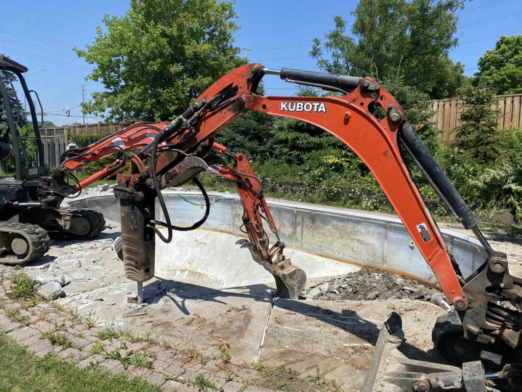 a kubota equipped with a jack-hammer breaking up a swimming pool and a digger picking up the debris