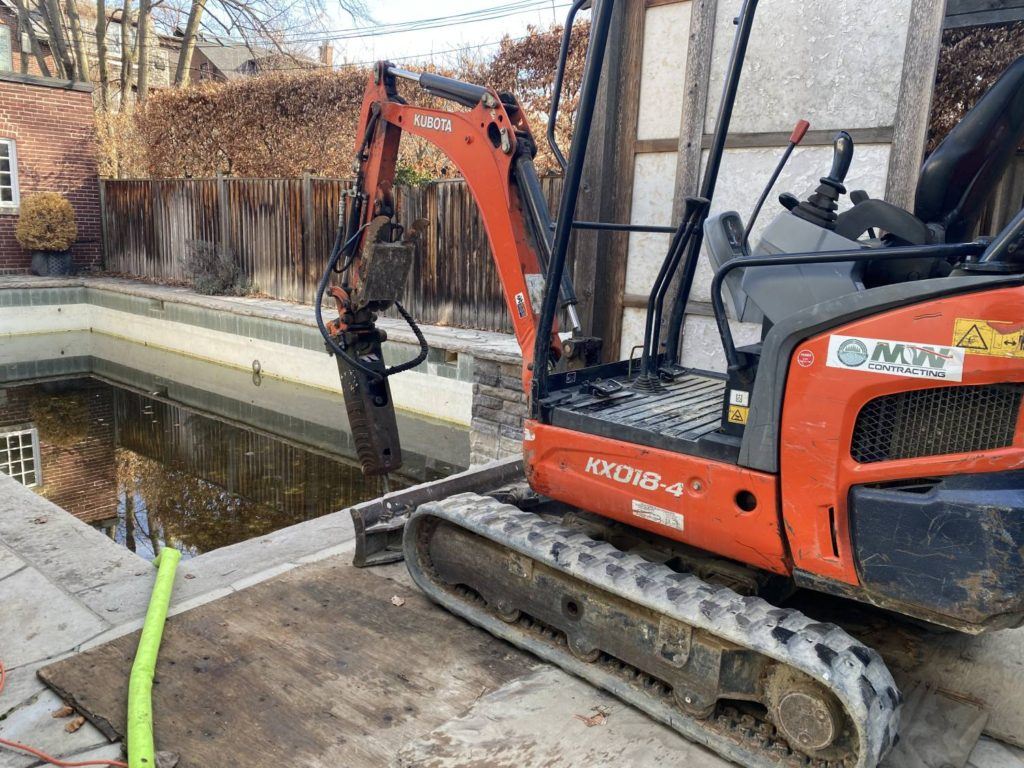 a kubota equipped with a jack-hammer breaking up a swimming pool