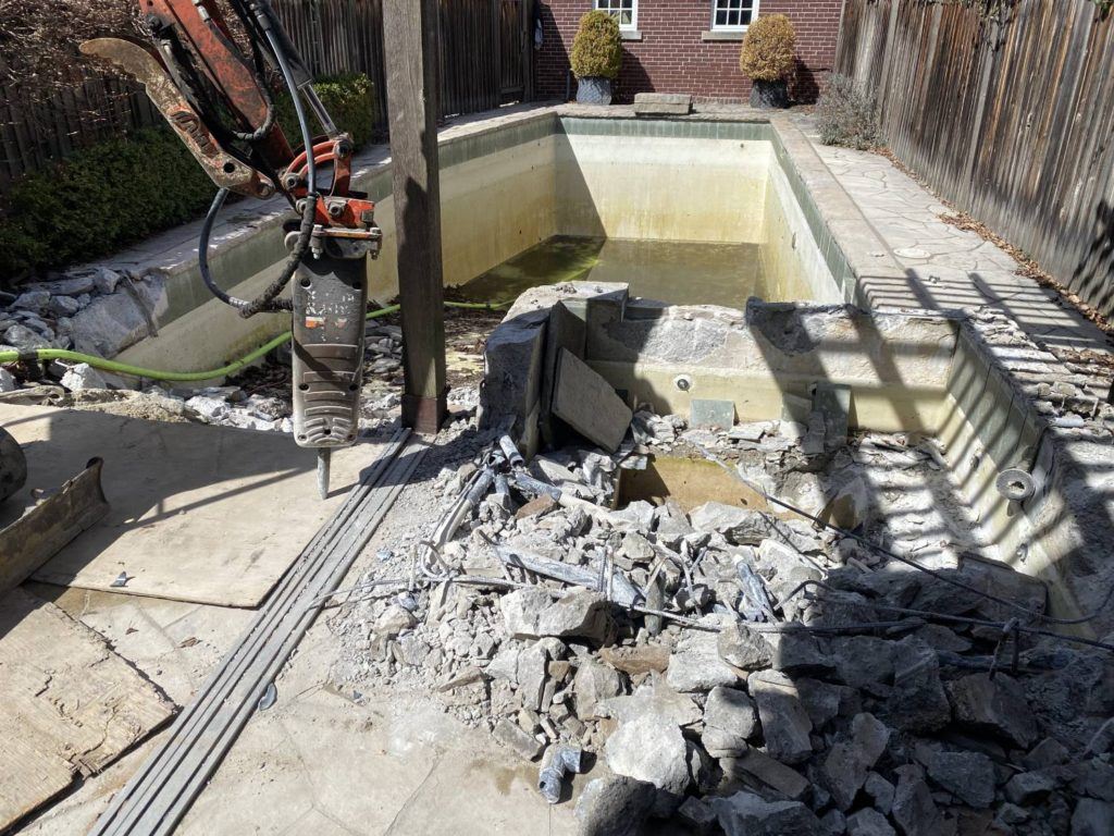 a kubota equipped with a jack-hammer breaking up a swimming pool