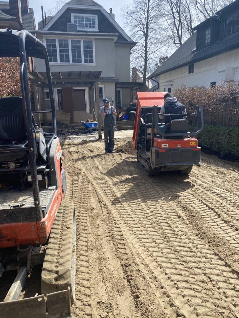 a man driving a kubota spreading sand in a garden