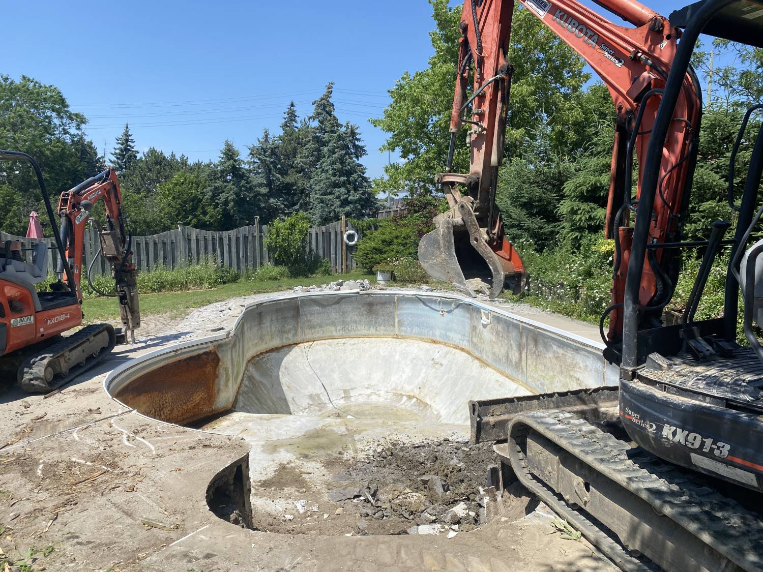 a kubota with a hammer attachment breaking up a swimming pool